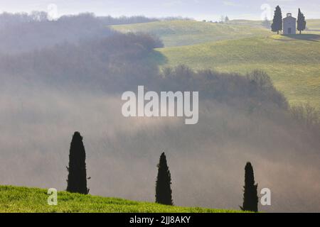 Toskanische Landschaft bei Sonnenaufgang mit berühmten Zypressen im nebligen grünen Tal und der kleinen Kapelle von Madonna di Vitaleta, San Quirico d'Orcia, Italien Stockfoto