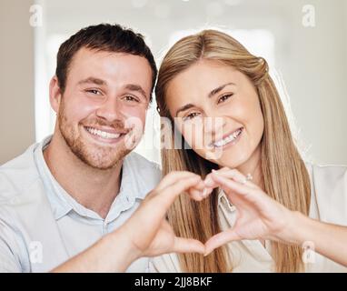 Sie sind ein Geschenk Gottes an Sie. Ein junges Paar, das mit den Händen zu Hause ein Herzzeichen macht. Stockfoto