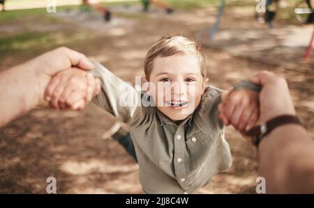 Das Gesicht des fröhlichen kaukasischen Jungen schwingt und dreht sich im Kreis der Arme im Park mit seinem Vater. Nettes verspieltes Kind, das Spaß beim Verbinden mit hat Stockfoto