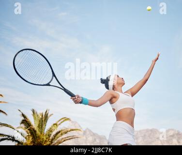 Heute arbeite ich an meinem Dienst. Junger Tennisspieler, der alleine auf dem Platz steht und während des Trainings den Ball bedient. Stockfoto