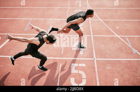 Um einen Zentimeter voraus. In einem hohen Winkel geschossen, als zwei hübsche junge Athleten während ihres Rennens auf einer Strecke die Ziellinie überquerten. Stockfoto