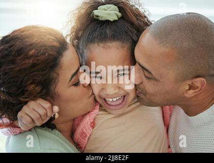 Ein entzückendes kleines Mädchen, das von ihren Eltern Küsse auf ihre Wangen bekommt. Stockfoto