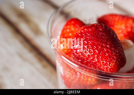 Nahaufnahme von Erdbeeren in einem Plastikbecher auf einem schäbigen Holztisch. Stockfoto