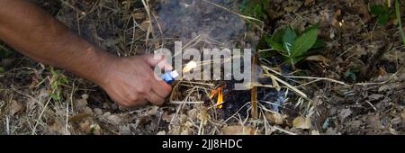 Bild der Hand eines Brandstifters, der mit einem Feuerzeug in einem Holz ein Feuer ausbricht. Hinweis auf das Problem der Waldbrände. Horizontales Banner Stockfoto