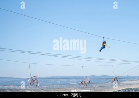 Glückliches Mädchen, das gegen den blauen Himmel gleitet oder Zipline klettert Stockfoto