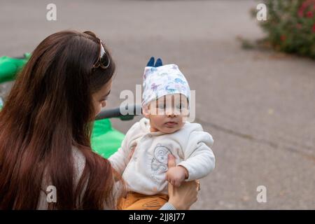 Junge Mutter hält unschuldiges Baby in liebevollen Händen draußen Stockfoto