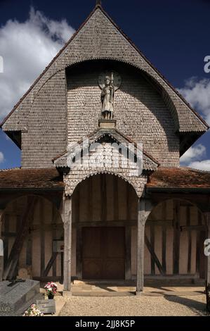 Der Apostel St. James der große steht auf den Besuchern von der Spitze der gefliesten und schindelten hölzernen Westveranda der Eglise Saint-Jacques-et-Saint-Philippe in Lentilles, in der Gegend Pays du der der Aube in Grand Est, Frankreich. Die um 1512 gegründete Kirche ist ein typisches Beispiel für die historischen Fachwerkkirchen oder Holzrahmen der Champagne-Region, mit massiven Eichenbalken, die ihre rot gefliesten Dächer stützen. Auch der Westgable und ein achteckiger Glockenturm sind von Holzschindeln umgeben. Stockfoto