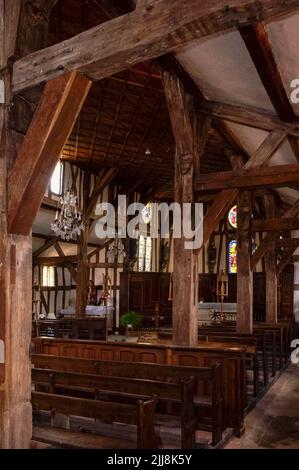 Kronleuchter und alte Buntglasfenster erhellen das himmlische Innere der Eglise Saint-Jacques-et-Saint-Philippe in Lentilles, in der Gegend Pays du der der Aube in Grand Est, Frankreich. Die um 1512 gegründete Kirche ist typisch für die holzgerahmten oder halbholzbedeckten Kirchen der Champagne-Region. Es verfügt über massive Eichensäulen und -Balken, die das Schifffahrtsschiff, Seitengänge und Chor stützen, und zahlreiche Buntglasfenster, darunter einige runde Öffnungen oder Oculi über den Buchten des Chors. Stockfoto