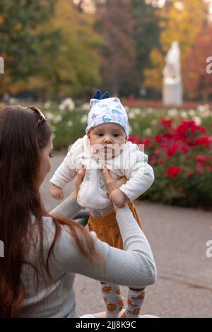 Mutter, die draußen im Park ein 6 Monate altes Baby in den Händen aufziehen ließ Stockfoto