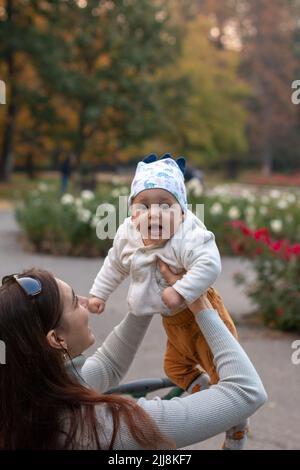 Die junge Mutter nimmt sich draußen im Park ein fröhliches Baby in den Armen Stockfoto