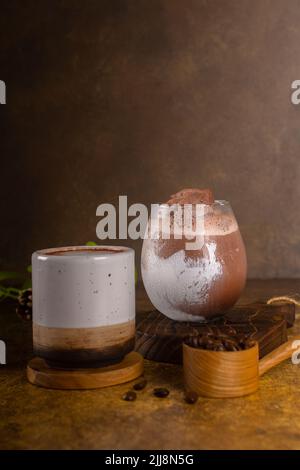 Schokoladengetränk mit Eis im Glas und heiß im Becher, auf rustikalem Holztablett und authentischem Hintergrund Stockfoto