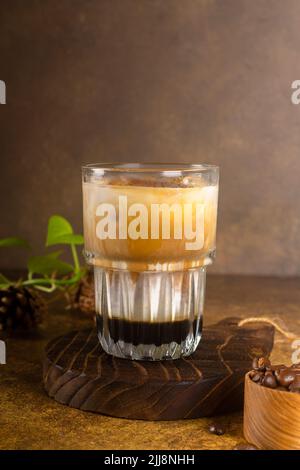 eiskaffee mit Kondensmilch auf rustikalem Holzuntersetzer und mit grünen Pflanzen, volle Kaffeebohne auf Vintage-Holzlöffel auf altem rustikalem Hintergrund Stockfoto