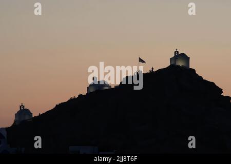 Touristen, die die malerischen kleinen Kapellen auf dem Hügel auf der atemberaubenden Insel iOS Greece erkunden, während die Sonne untergeht Stockfoto