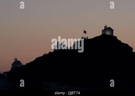 Touristen, die die malerischen kleinen Kapellen auf dem Hügel auf der atemberaubenden Insel iOS Greece erkunden, während die Sonne untergeht Stockfoto