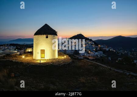 Blick auf eine schöne beleuchtete weiße Windmühle, während die Sonne dramatisch hinter dem Dorf iOS in Griechenland untergeht Stockfoto