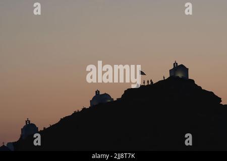 Touristen, die die malerischen kleinen Kapellen auf dem Hügel auf der atemberaubenden Insel iOS Greece erkunden, während die Sonne untergeht Stockfoto