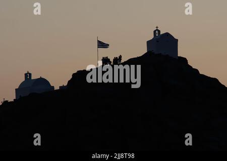 Touristen, die die malerischen kleinen Kapellen auf dem Hügel auf der atemberaubenden Insel iOS Greece erkunden, während die Sonne untergeht Stockfoto