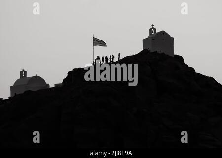 Touristen erkunden die malerischen kleinen Kapellen auf der atemberaubenden Insel iOS Greece, während die Sonne schwarz-weiß untergeht Stockfoto