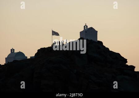 Touristen, die die malerischen kleinen Kapellen auf dem Hügel auf der atemberaubenden Insel iOS Greece erkunden, während die Sonne untergeht Stockfoto