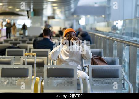 Afrikanischer Reisender Mann trinkt Kaffee und wartet auf den Flug am Flughafenterminal, spricht mit dem Handy. Stockfoto