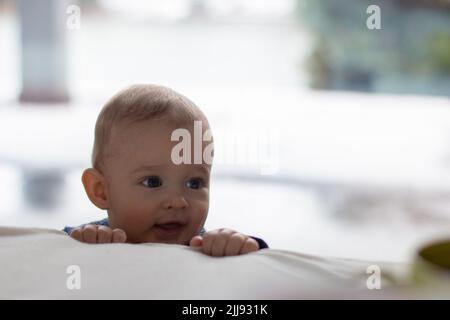 Neugieriges Kleinkind, das über dem Bett aufwacht, niedliches spitzbübisch kaukasisches blondes Baby Junge Stockfoto