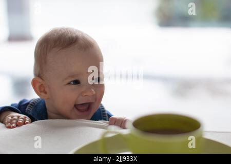 Lachend schelmisch Kleinkind mit einem niedlichen frechen Ausdruck, kleiner blonder Junge Unruhestifter, tägliche häusliche Leben Kindheitsszene Stockfoto