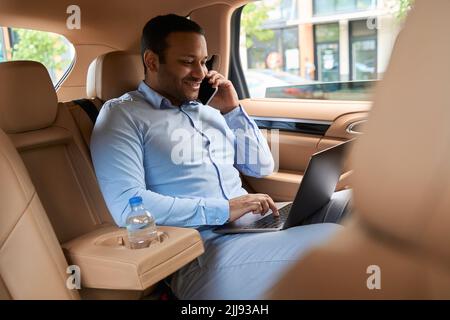 Junger Geschäftsmann, der im Auto am Computer arbeitet Stockfoto