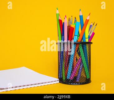 Buntstifte in einer Stiftetui auf gelbem Grund mit einem weißen Blatt Papier Stockfoto