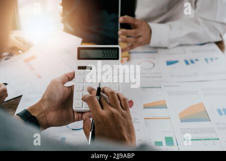 asiatischer Geschäftsmann oder Buchhalter, der mit Zeigegraphen für Diskussionen und Analysen arbeitet, Datendiagramme und -Grafiken erstellt und Zahlen mit einem Rechner berechnet Stockfoto