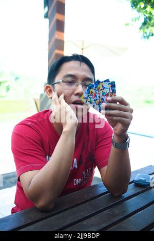 Porträt eines jungen und hübschen asiatischen Mannes, der im Pokerspiel auf einem Holztisch sitzt und Karten hält. Ernsthafter Ausdruck. Stockfoto