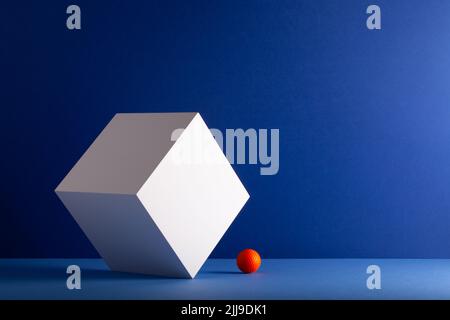Weißer Würfel mit orangefarbenem Golfball auf blauem Hintergrund. Kreatives Bild. Stockfoto