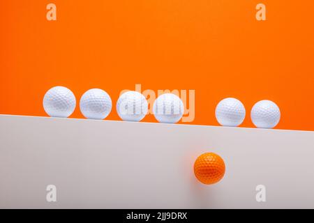 Weiße Golfbälle an der Wand. Ein orangefarbener Golfball fällt die Wand herunter. Sportkonzept und Idee Stockfoto