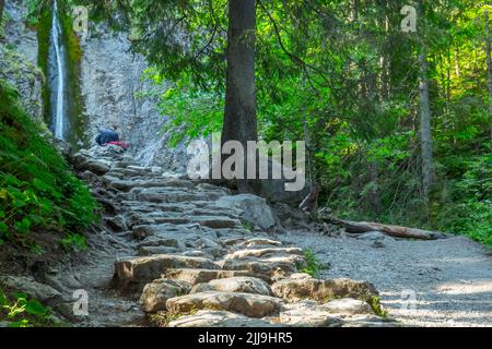 Wandern auf den Bergwegen. Strazyska-Tal, Tatra-Gebirge. Steinpfad, Bergwasserfall in der Ferne. Stockfoto