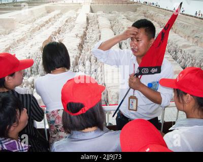 Besorgt aussehender Reiseführer mit knallfarbener Flagge, vielleicht schwer denkend, eine harte Frage zu beantworten oder in einer stressigen Situation, führt eine Gruppe chinesischer Touristen an, die die Grube 1 der Terrakotta-Armee im Mausoleum-Museum von Kaiser Qinshihuang in Xi'an, China, besuchen/besichtigen. VRC. (125) Stockfoto