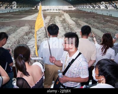 Reiseleiter mit knallfarbener Flagge führt eine Gruppe chinesischer Touristen an, die die Grube 1 der Terrakotta-Armee im Mausoleum-Museum von Kaiser Qinshihuang in Xi'an, China, besuchen/besichtigen. VRC. (125) Stockfoto