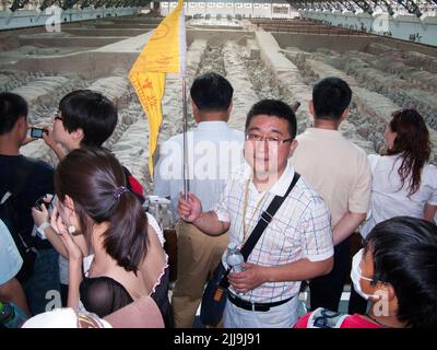 Reiseleiter mit knallfarbener Flagge führt eine Gruppe chinesischer Touristen an, die die Grube 1 der Terrakotta-Armee im Mausoleum-Museum von Kaiser Qinshihuang in Xi'an, China, besuchen/besichtigen. VRC. (125) Stockfoto