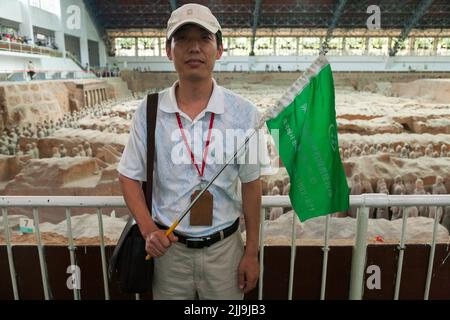 Reiseleiter mit knallfarbener Flagge führt eine Gruppe chinesischer Touristen an, die die Grube 1 der Terrakotta-Armee im Mausoleum-Museum von Kaiser Qinshihuang in Xi'an, China, besuchen/besichtigen. VRC. (125) Stockfoto