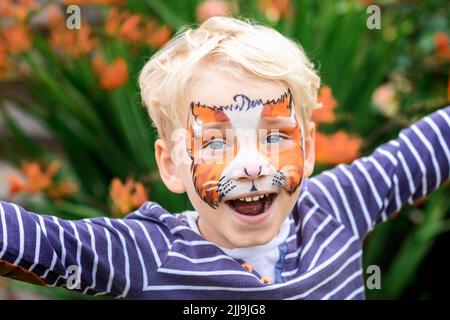 Netter glücklicher und aufgeregt kleiner Junge mit Gesichtsfarbe. Gesichtsbemalung, Kindergesicht auf der Geburtstagsparty oder an Feiertagen Stockfoto