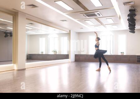 Eine anmutige Balletttänzerin in einem schwarzen Tutu führt Ballettübungen vor einem Spiegel im Studio durch Stockfoto