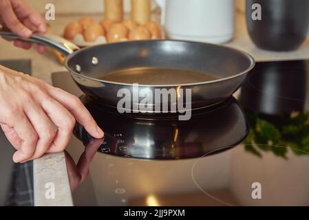 Modernes Küchengerät, mit der Hand der Frau am Induktionsherd mit Bratpfanne aus Stahl, Sensortaste mit Finger am Induktions- oder Elektroherd Stockfoto