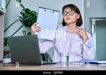 Frau mittleren Alters, die an Hitze leidet, überhitzt, durch Ventilator und Ventilator gekühlt Stockfoto