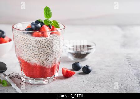 Chia-Erdbeerpudding. Gesundes veganes Frühstück Chiasamen Pudding mit frischen Beeren und Minze im Glas auf grauem Betongrund. Konzept des Gesundheitsgedankens Stockfoto