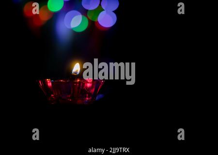 Diwali Diya aus Glas in roter Farbe mit buntem Bokeh auf dem Hintergrund mit dunkelschwarzer Farbe und Kopierraum für Text. Stockfoto