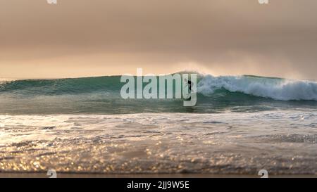 Surfer reitet von einer kleineren Welle am Strand am atlantischen Ozean Stockfoto