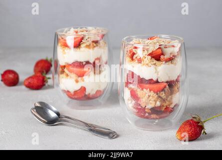 Erdbeerdessert in Gläsern mit Keks, Mascarpone-Käse und Mandeln. Köstliches Dessert für Kinderparty auf grauem Hintergrund Stockfoto