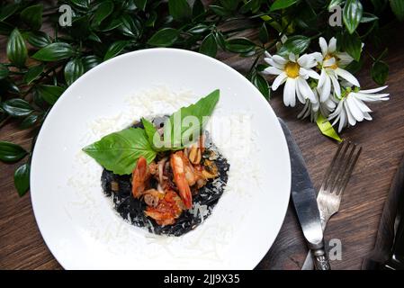 Ein Teller Pasta mit Tintenfisch und Meeresfrüchten, unter geriebenem Parmesankäse, garniert mit frischen Basilikumblättern. Draufsicht. Stockfoto