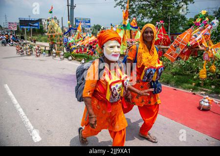 Kanwariya sah, wie sie eine Narendra Modi Maske trug und während des jährlichen Kanwar Yatra vor dem Shivratri Festival auf der Delhi Meerut Road, Ghaziabad, heiliges Wasser trug. Der Monat Sravana (der vierte Monat des Hindu-Kalenders) ist Lord Shiva gewidmet. Während der jährlichen Monsunsaison tragen Tausende von safrangekleideten Pilgern Wasser aus dem Ganges in Haridwar, Gangotri oder Gaumukh und kehren in ihre Heimatorte zurück, wo sie später als Dankesgeste Abhisheka (Salbung) der Shivalingas in den lokalen Shiva-Tempeln durchführen. Stockfoto