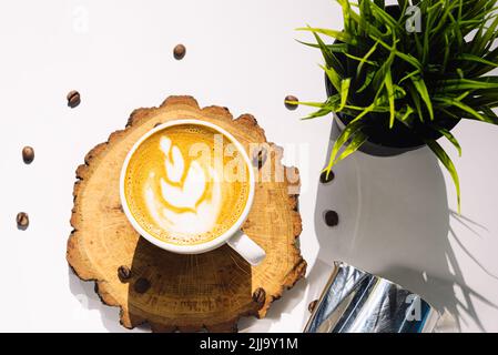 Eine Tasse Cappuccino auf einem Holzbrett. Blumenzeichnung auf einem Kaffeeschaum. Blick von oben. Hartes Licht von der hellen Sommersonne. Stockfoto