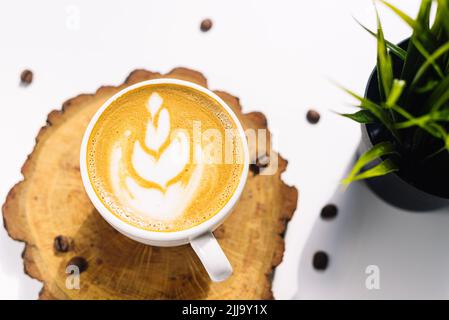 Eine Tasse Cappuccino auf einem Holzbrett. Blumenzeichnung auf einem Kaffeeschaum. Blick von oben. Hartes Licht von der hellen Sommersonne. Stockfoto