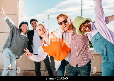 Fünf multiethnische Freunde posieren vor der Kamera lächelnd und haben gemeinsam Spaß im Freien. Stockfoto